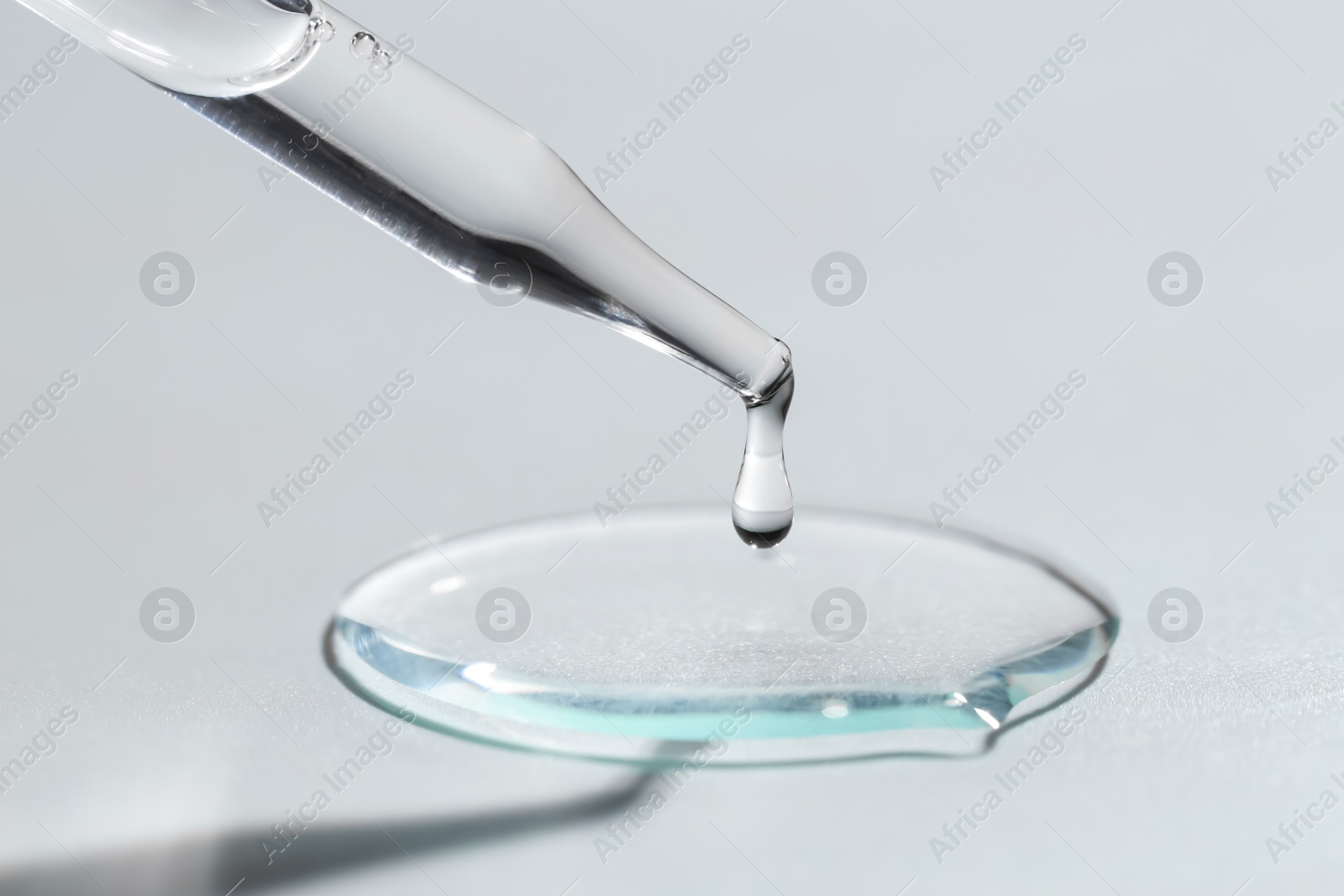 Photo of Dripping cosmetic serum from pipette on light background, closeup