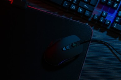 Photo of Computer mouse, mousepad and keyboard on dark wooden table in neon lights, flat lay