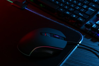 Photo of Computer mouse, mousepad and keyboard on dark wooden table in neon lights, closeup