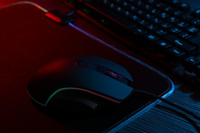 Photo of Computer mouse, mousepad and keyboard on dark wooden table in neon lights, closeup