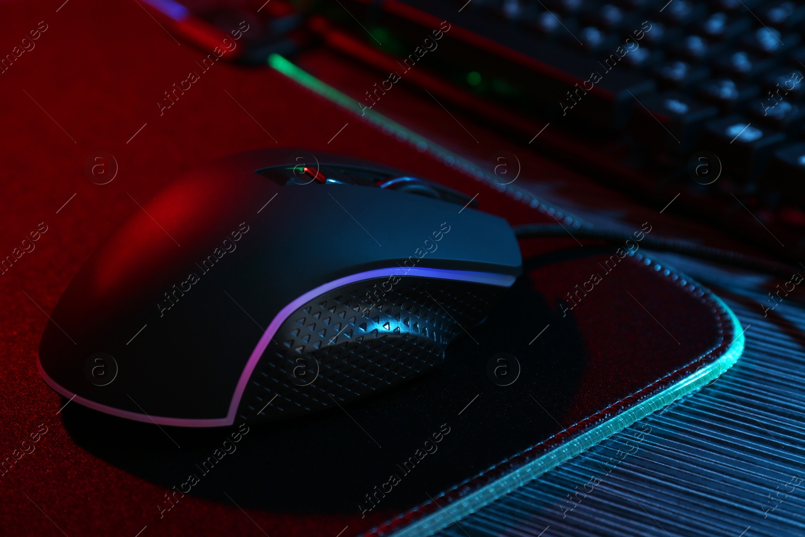 Photo of Computer mouse and mousepad on dark wooden table in neon lights, closeup