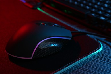 Photo of Computer mouse and mousepad on dark wooden table in neon lights, closeup