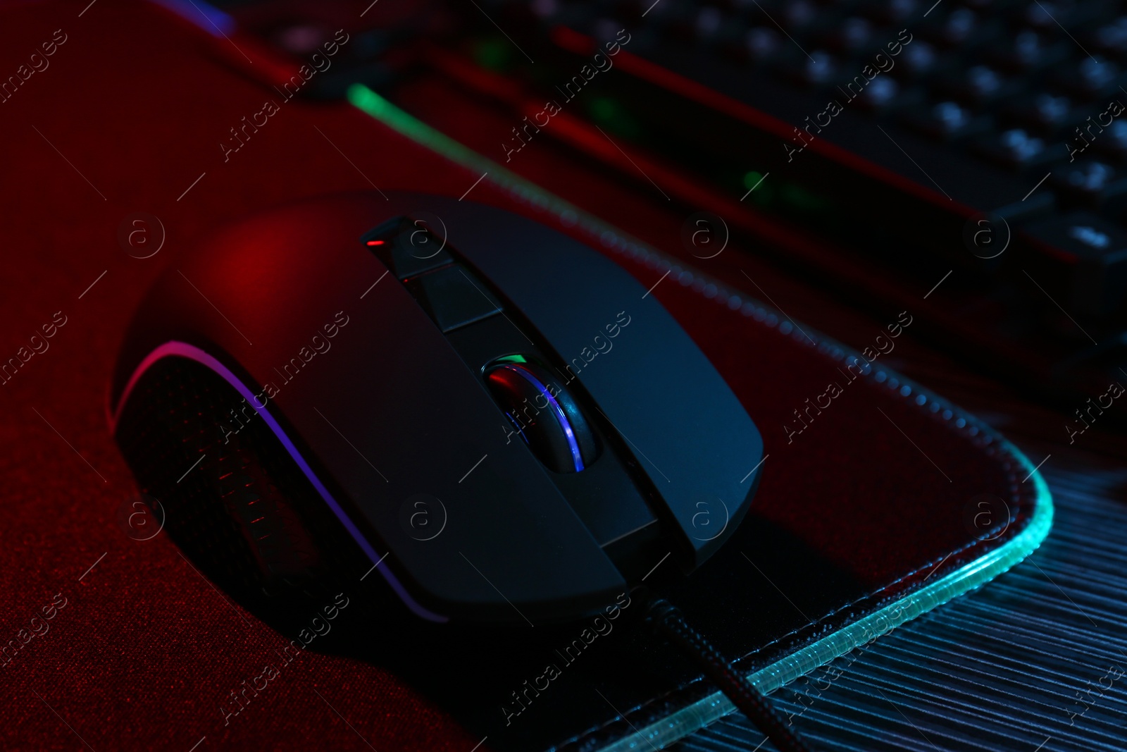 Photo of Computer mouse and mousepad on dark wooden table in neon lights, closeup