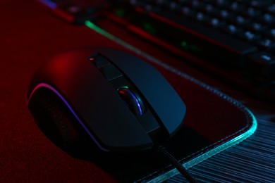 Photo of Computer mouse and mousepad on dark wooden table in neon lights, closeup