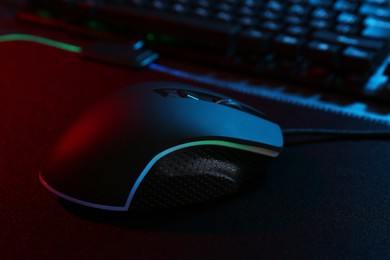 Photo of Computer mouse and mousepad on table in neon lights, closeup