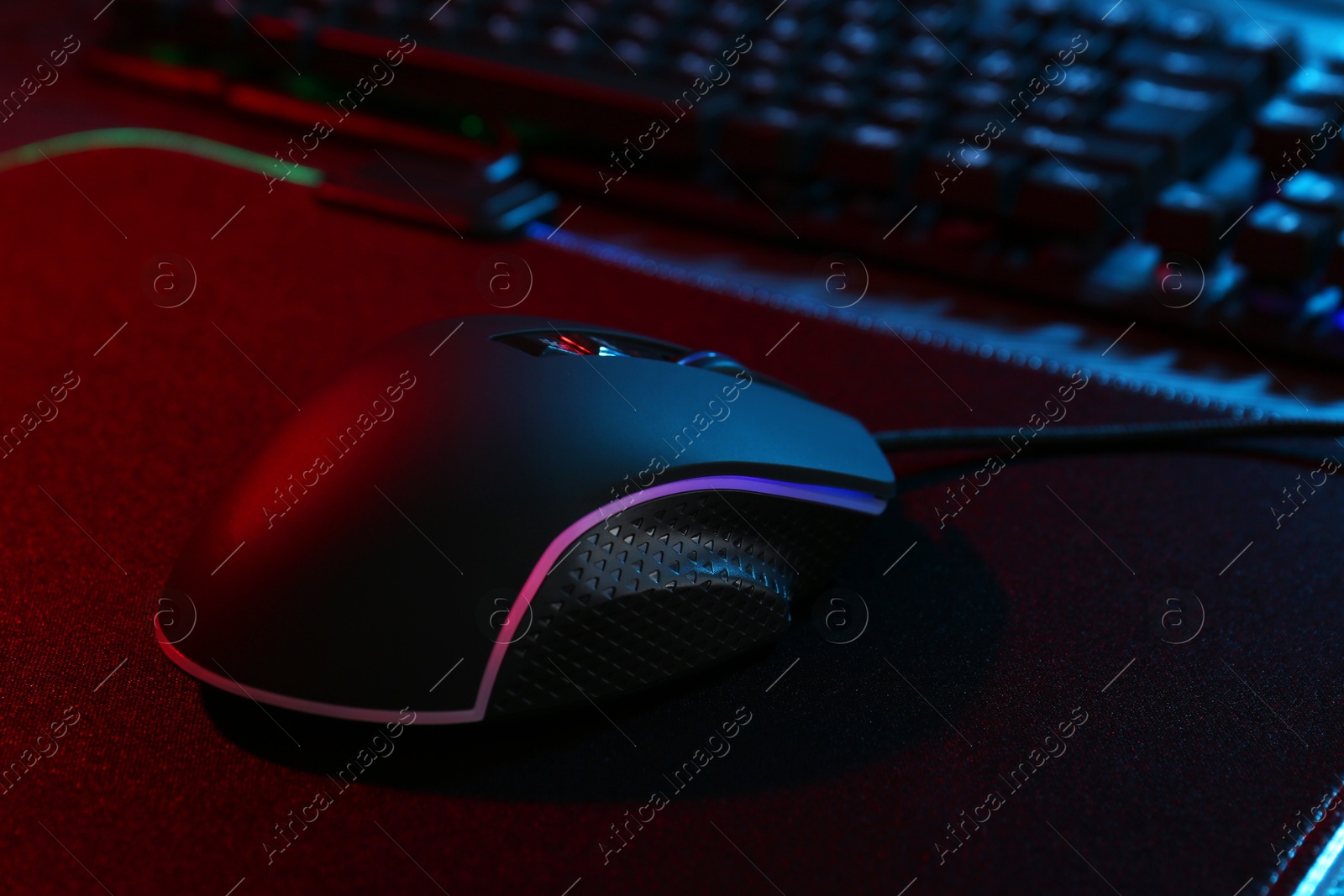 Photo of Computer mouse and mousepad on table in neon lights, closeup