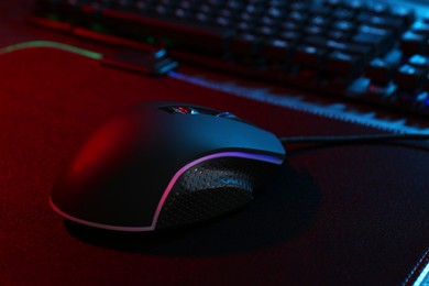 Photo of Computer mouse and mousepad on table in neon lights, closeup