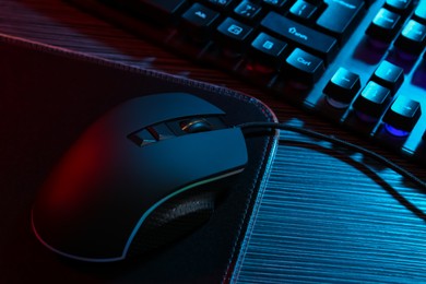 Photo of Computer mouse, mousepad and keyboard on dark wooden table in neon lights, closeup