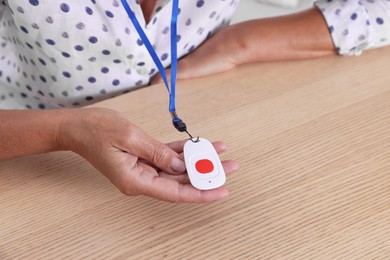 Senior woman with emergency call button at wooden table, closeup