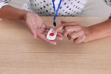 Photo of Senior woman pressing emergency call button at wooden table, closeup