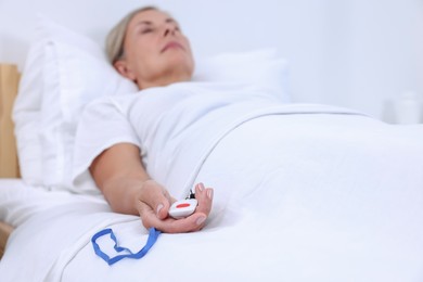 Photo of Senior woman with emergency call button on bed in hospital, selective focus