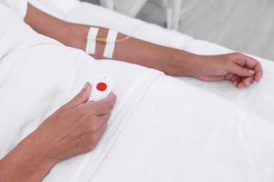 Photo of Senior woman with emergency call button on bed in hospital, closeup