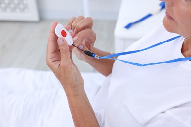 Senior woman pressing emergency call button on bed in hospital, closeup