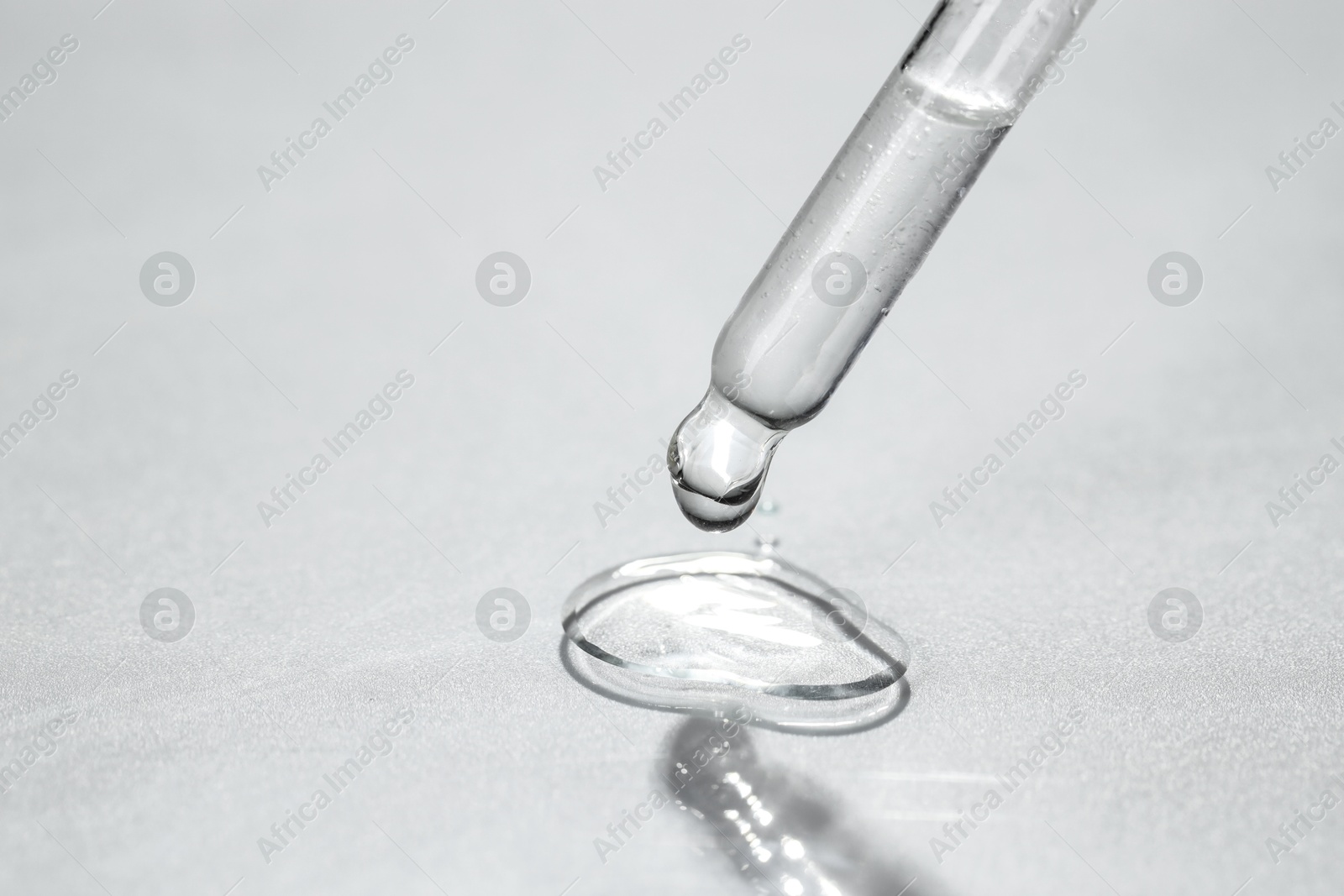 Photo of Cosmetic oil dripping from pipette on light grey background, closeup