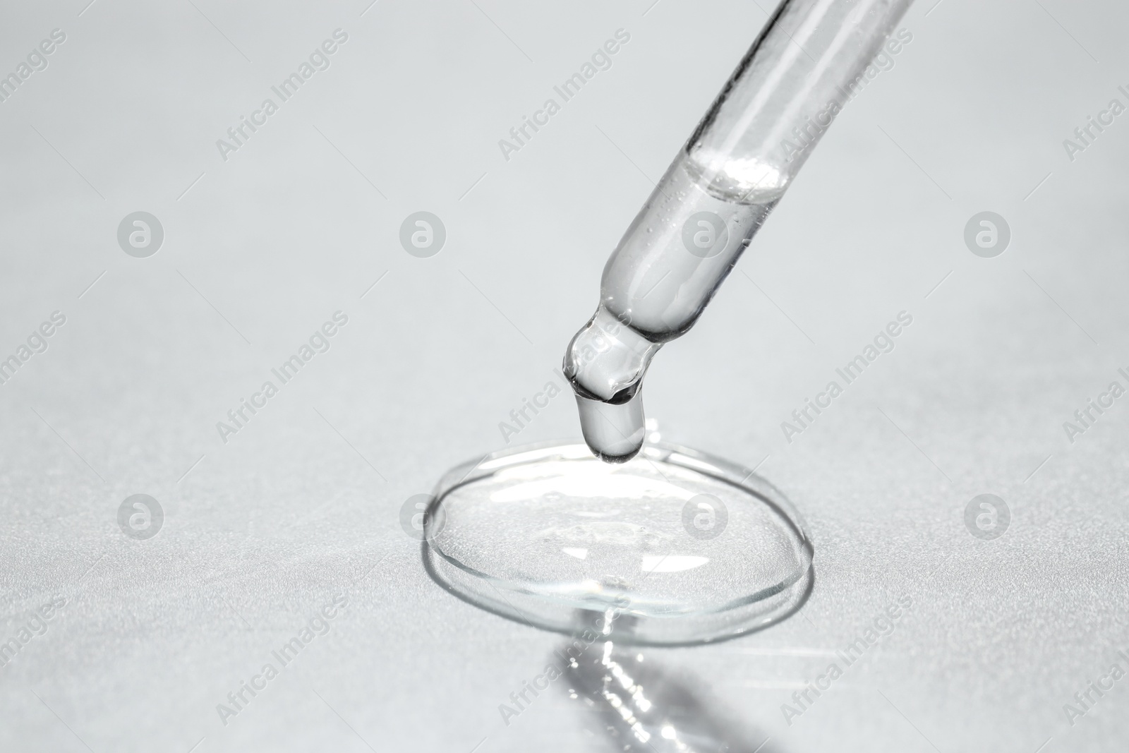 Photo of Cosmetic oil dripping from pipette on light grey background, closeup