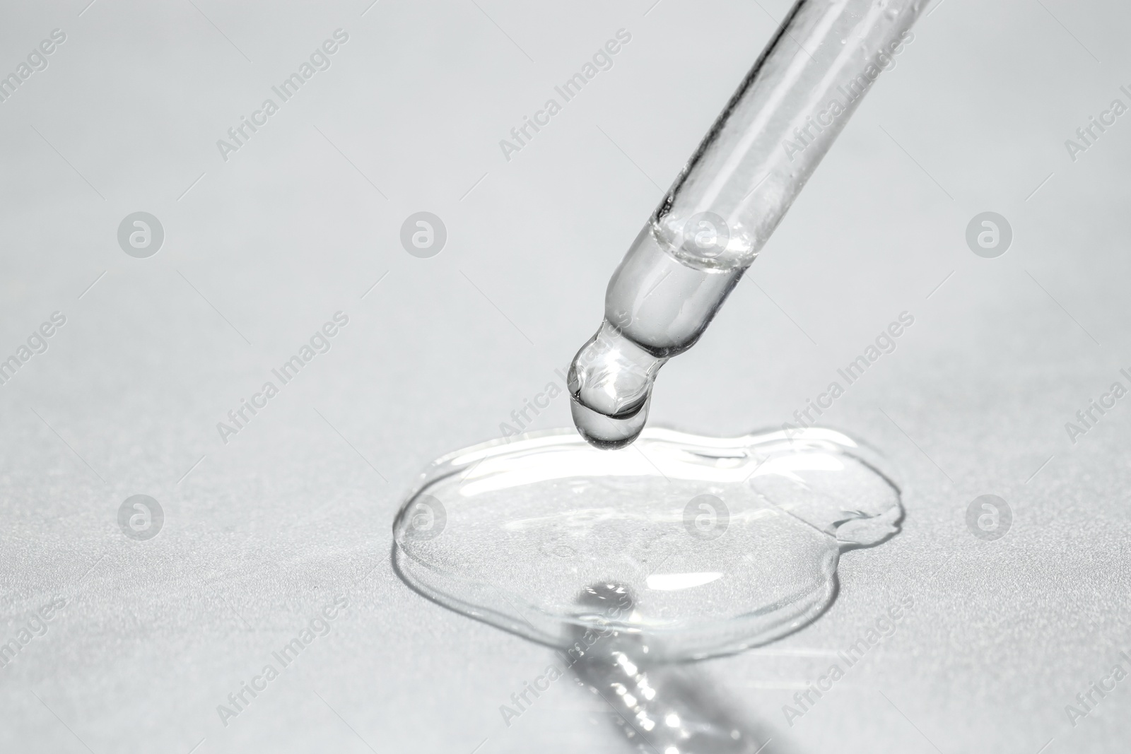 Photo of Cosmetic oil dripping from pipette on light grey background, closeup