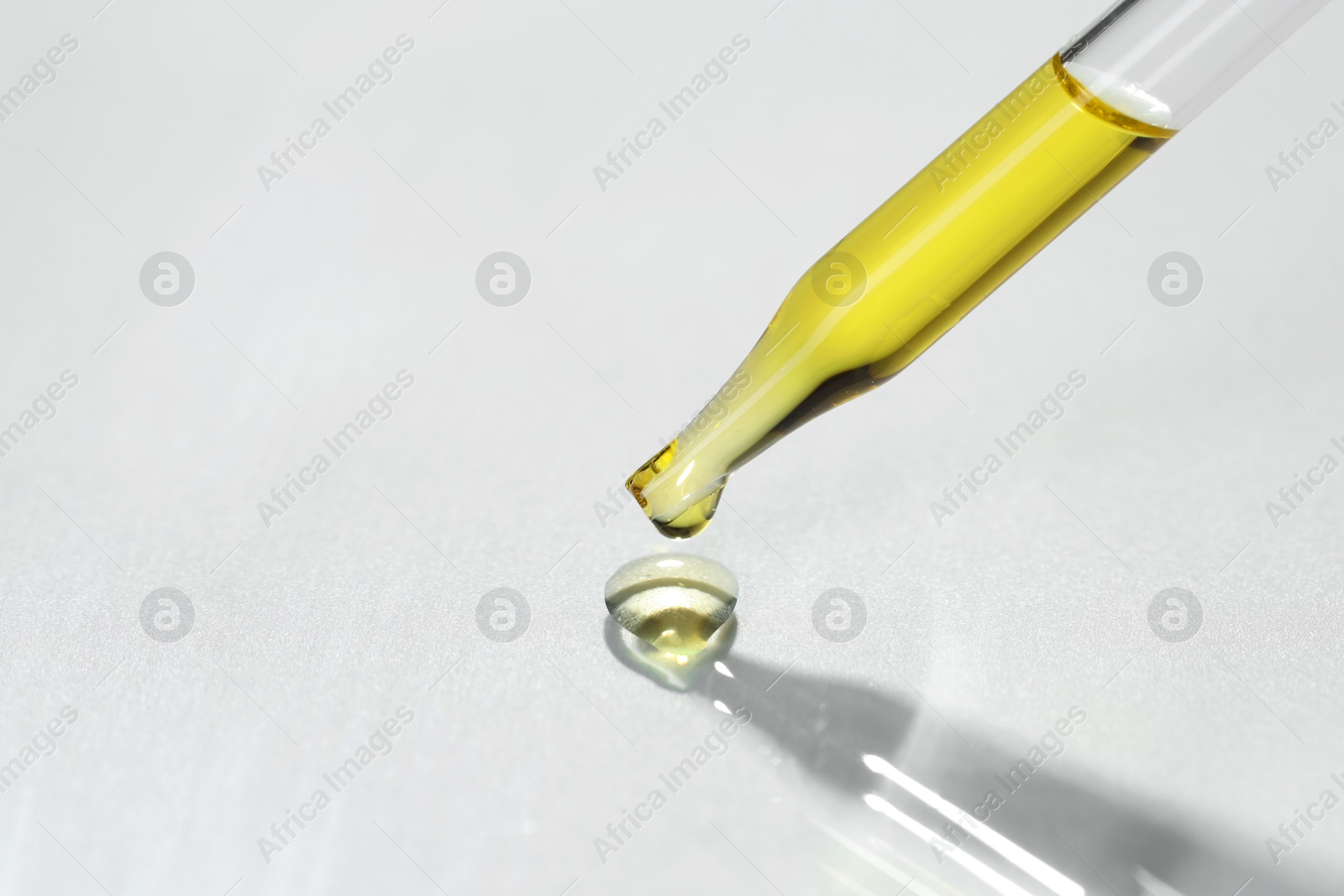 Photo of Cosmetic oil dripping from pipette on light grey background, closeup