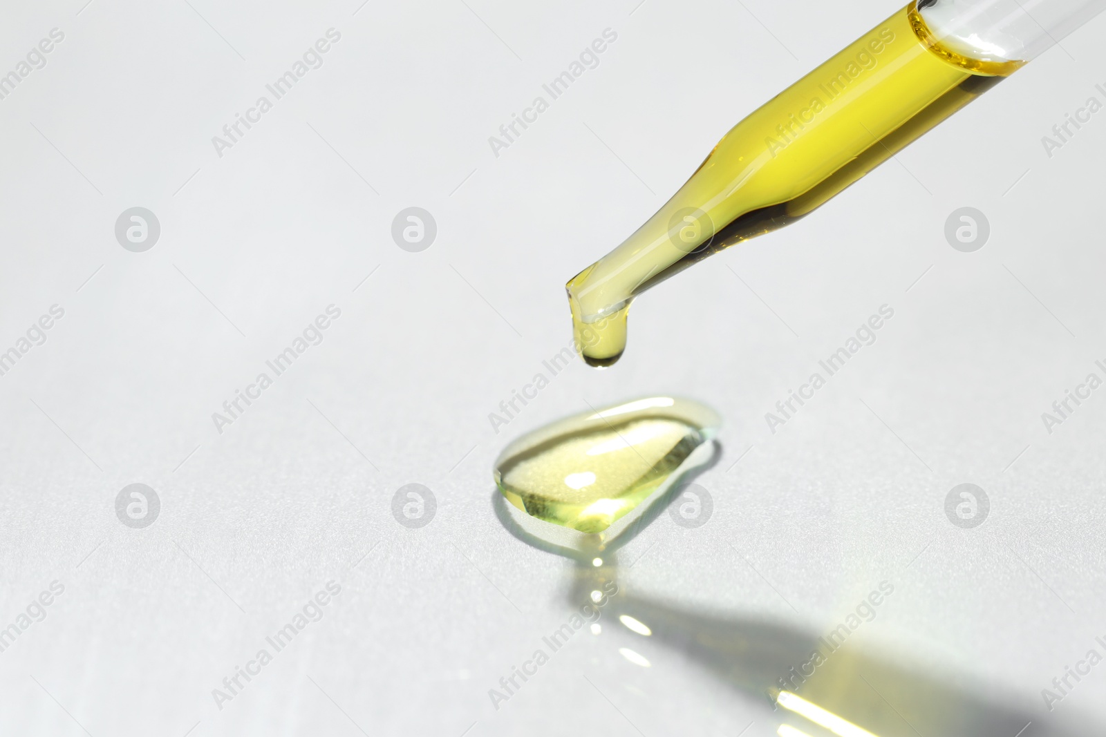 Photo of Cosmetic oil dripping from pipette on light grey background, closeup