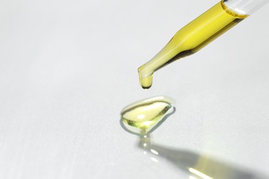 Cosmetic oil dripping from pipette on light grey background, closeup