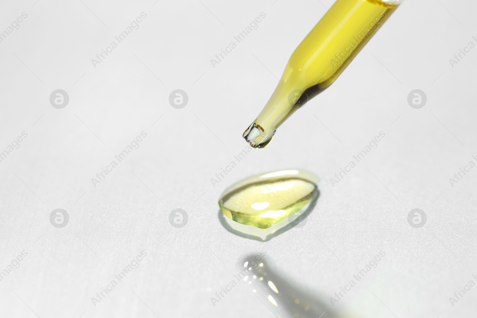 Photo of Cosmetic oil dripping from pipette on light grey background, closeup