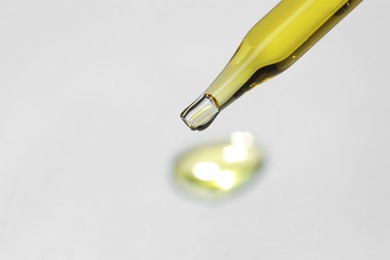 Photo of Cosmetic oil dripping from pipette on light grey background, closeup