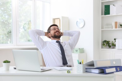 Smiling businessman sitting at table in office with hands behind his head. Break time