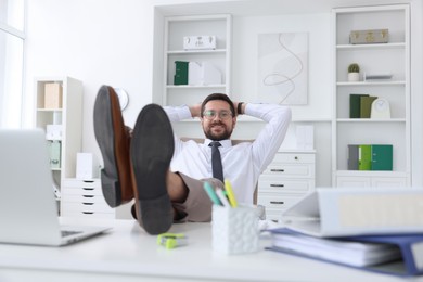 Photo of Smiling businessman with hands behind his head holding legs on table in office. Break time