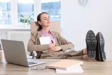 Beautiful businesswoman with notebook and pen holding legs on table in office. Break time