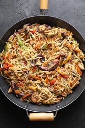 Photo of Stir-fry noodles with sea food and vegetables in wok on dark textured table, top view