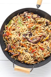 Photo of Stir-fry noodles with sea food and vegetables in wok on white wooden table, top view