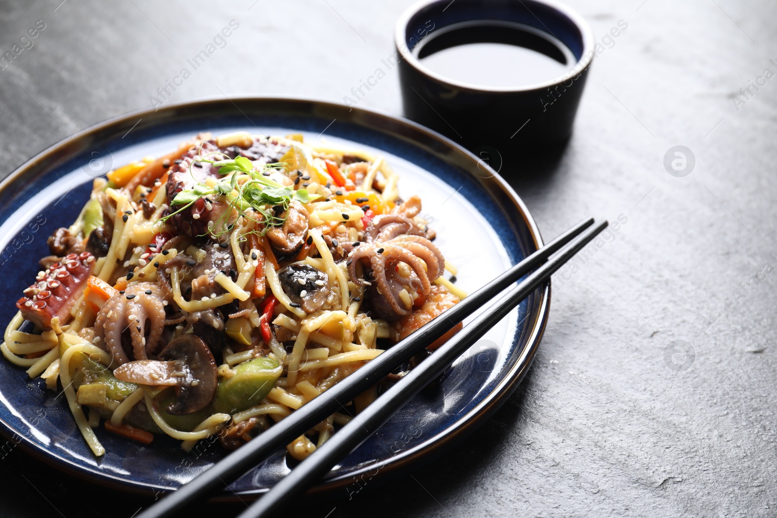 Photo of Stir-fry noodles with sea food, vegetables and soy sauce on dark textured table, closeup