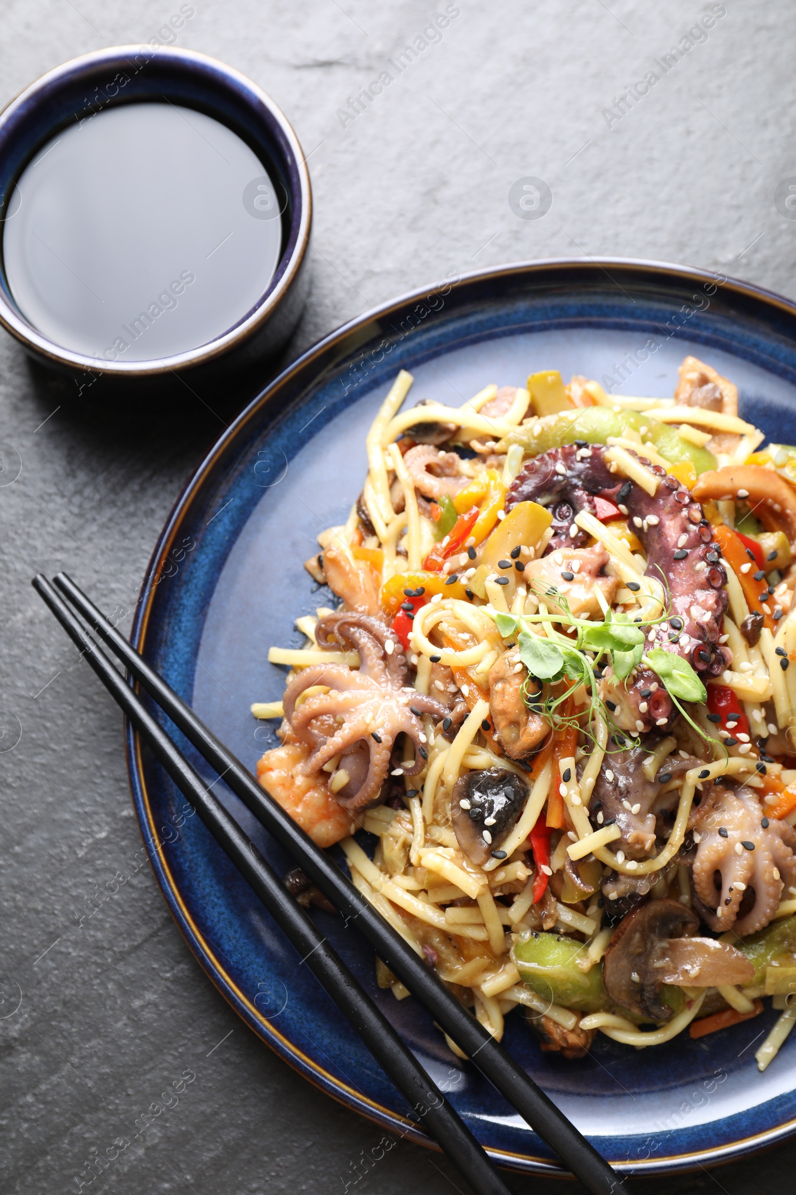 Photo of Stir-fry noodles with sea food, vegetables and soy sauce on dark textured table, top view