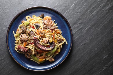 Photo of Stir-fry noodles with sea food and vegetables on dark textured table, top view. Space for text