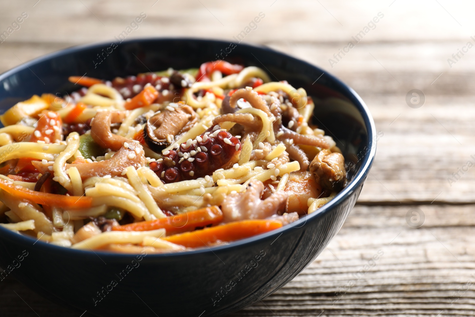 Photo of Stir-fry noodles with sea food and vegetables on wooden table, closeup