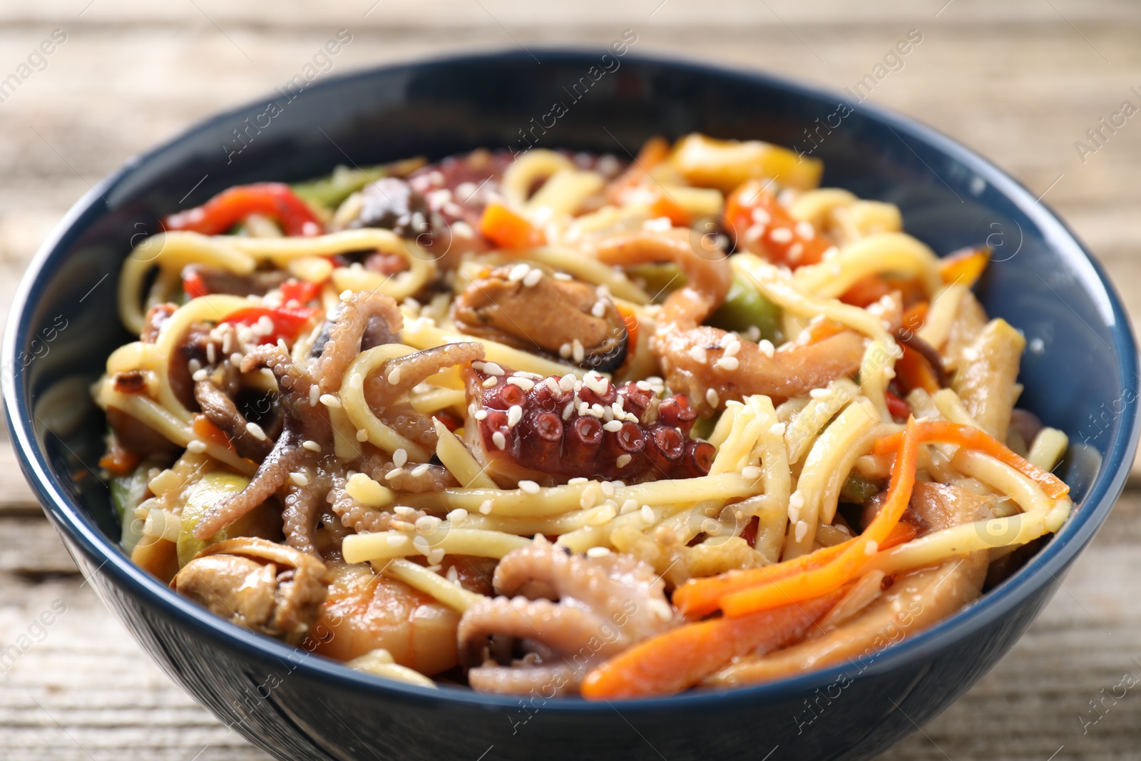 Photo of Stir-fry noodles with sea food and vegetables on wooden table, closeup