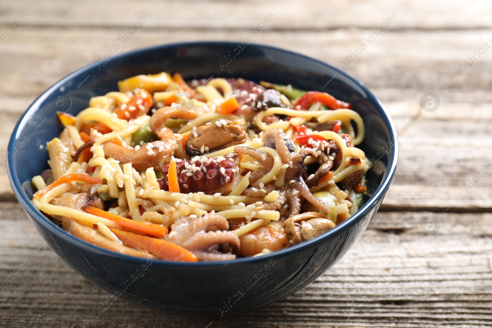 Photo of Stir-fry noodles with sea food and vegetables on wooden table, closeup