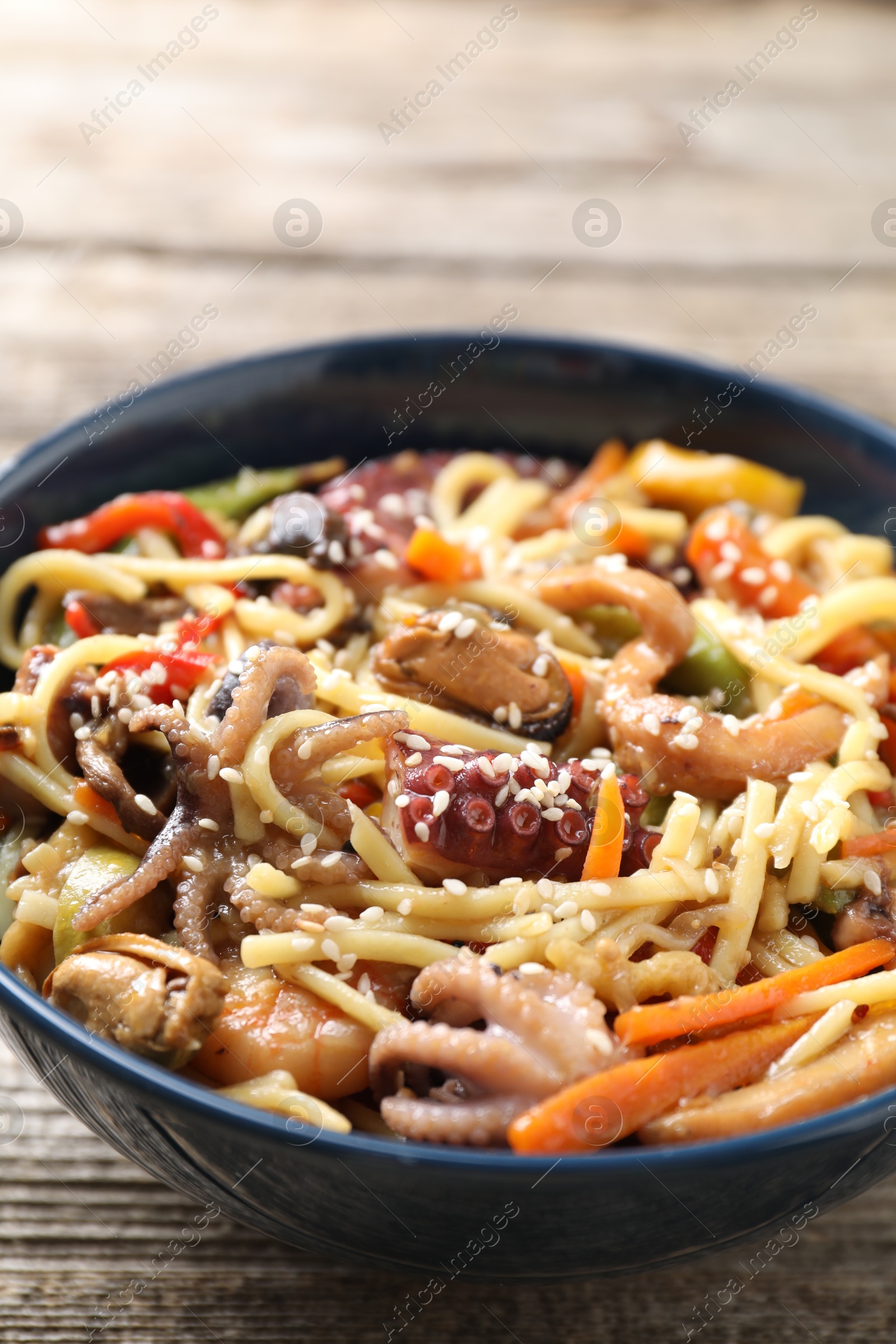 Photo of Stir-fry noodles with sea food and vegetables on wooden table, closeup