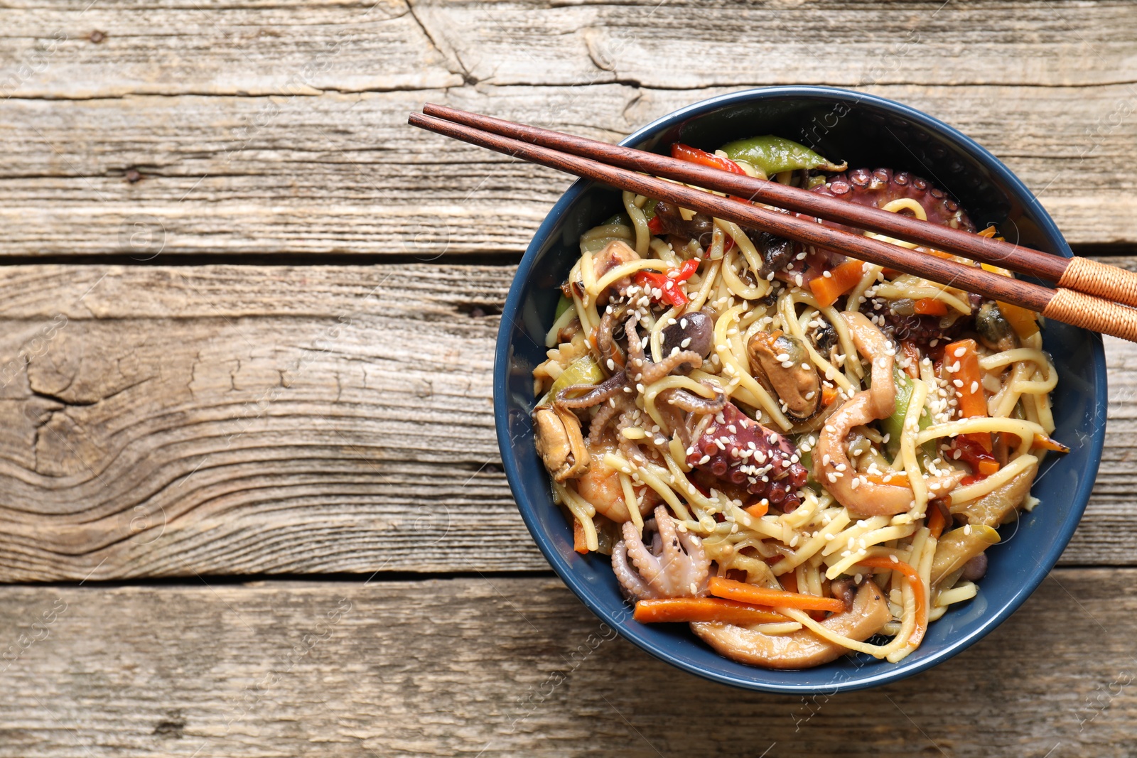 Photo of Stir-fry noodles with sea food and vegetables on wooden table, top view. Space for text