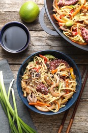 Photo of Stir-fry noodles with sea food and vegetables served on wooden table, flat lay