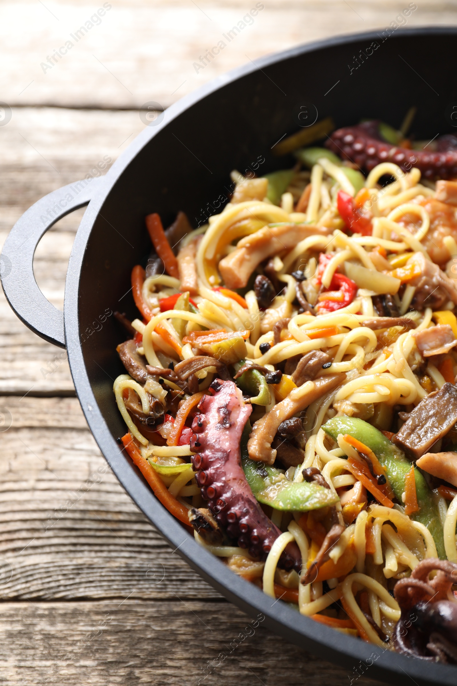 Photo of Stir-fry noodles with sea food and vegetables in wok on wooden table, closeup