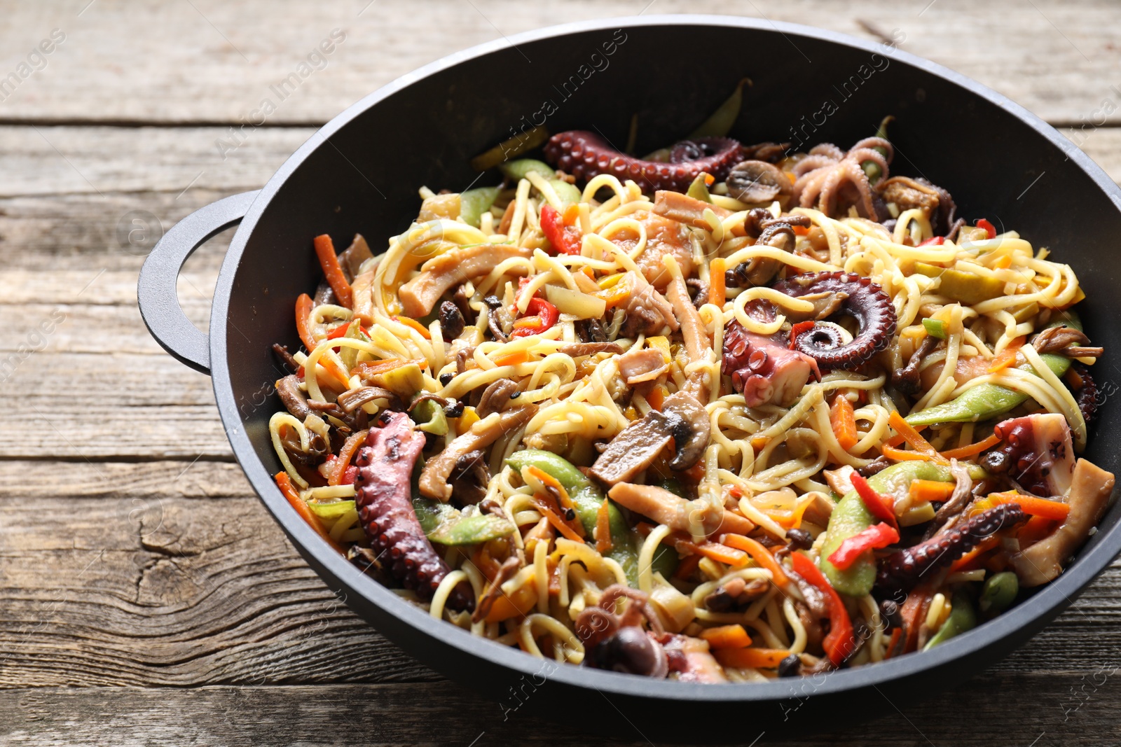 Photo of Stir-fry noodles with sea food and vegetables in wok on wooden table, closeup