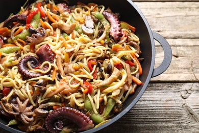 Stir-fry noodles with sea food and vegetables in wok on wooden table, closeup