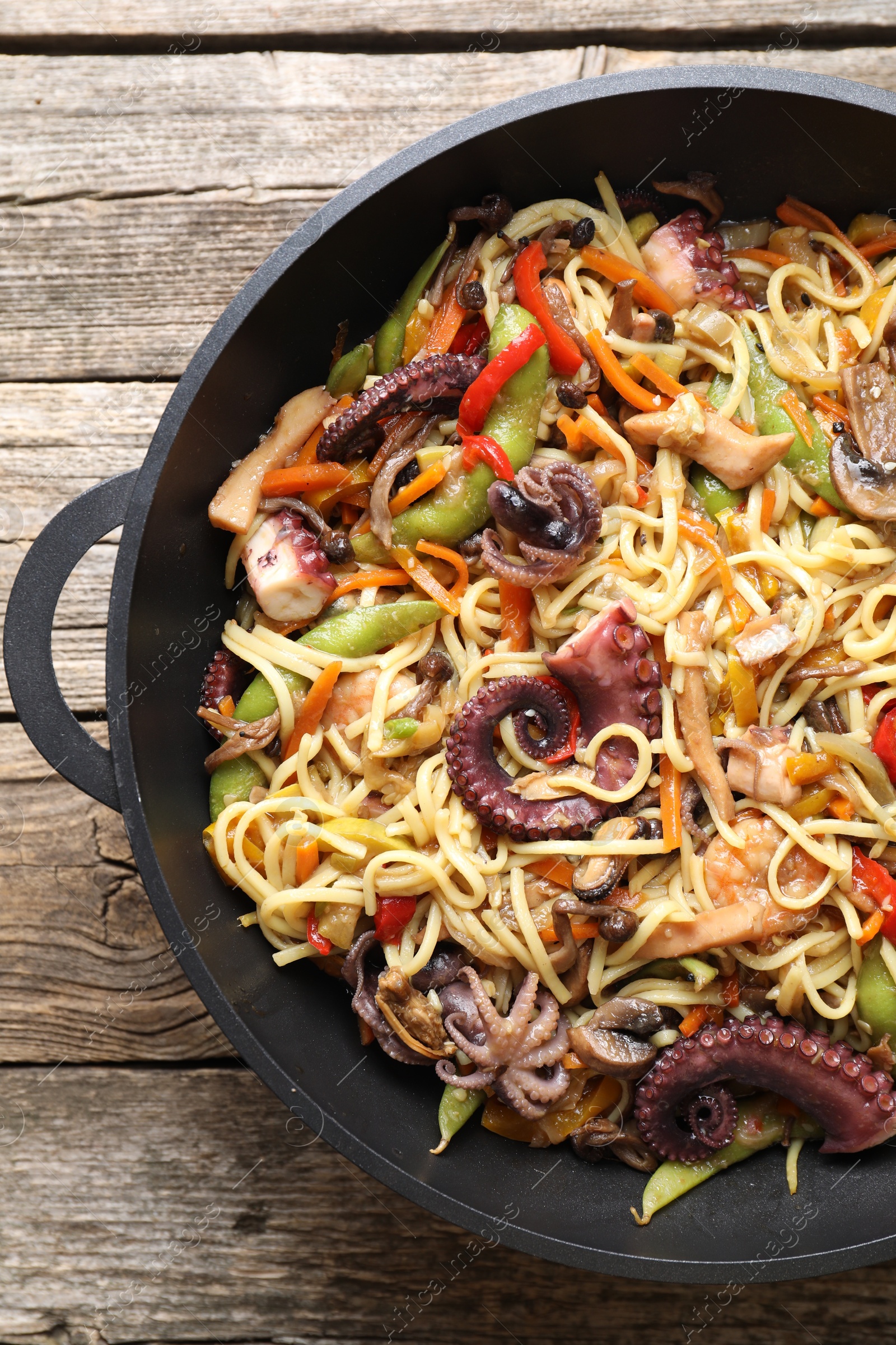 Photo of Stir-fry noodles with sea food and vegetables in wok on wooden table, top view