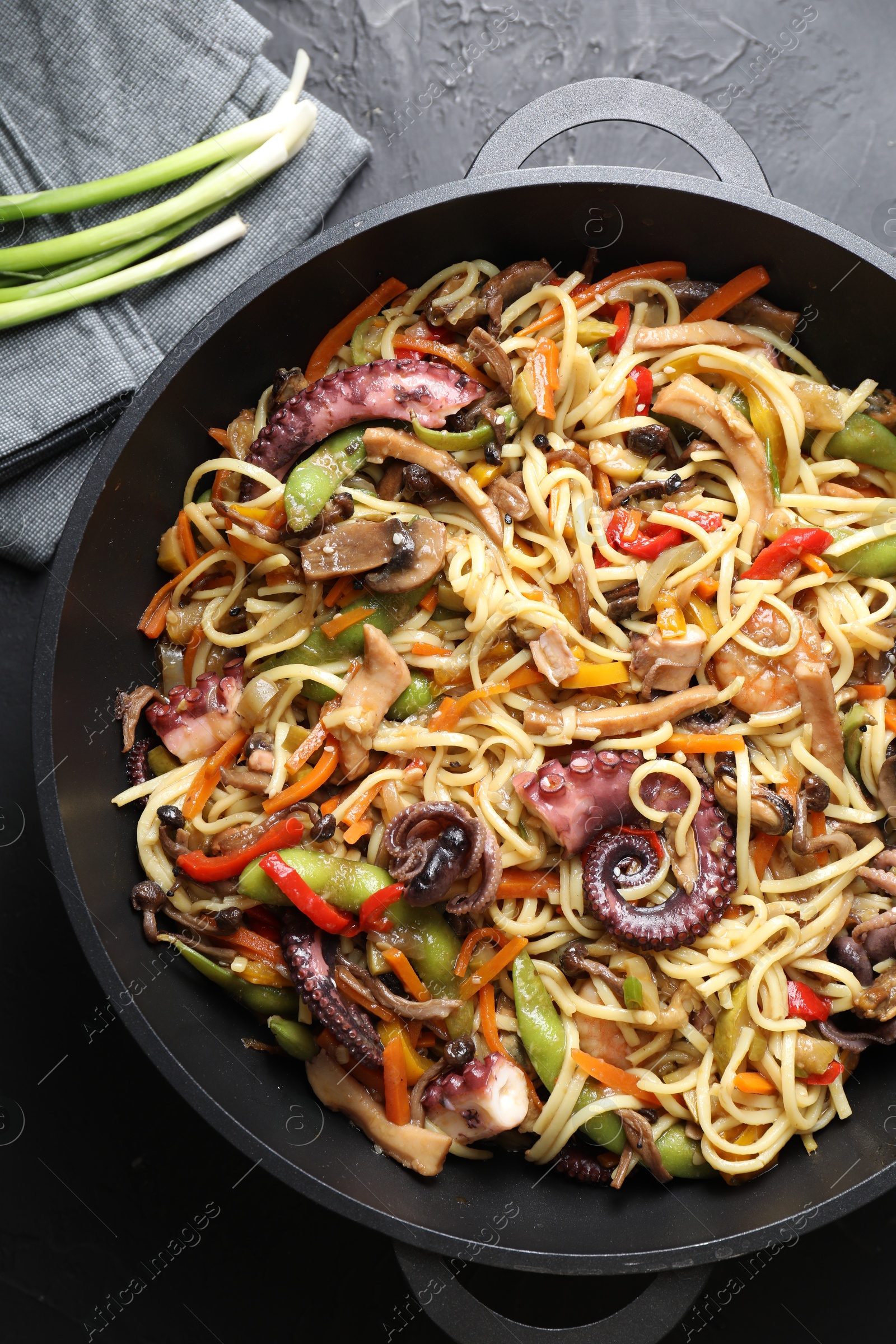 Photo of Stir-fry noodles with sea food and vegetables in wok on dark textured table, top view