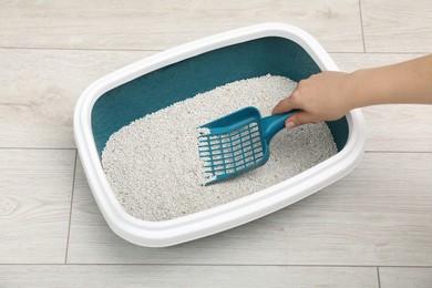 Woman cleaning cat litter tray indoors, closeup