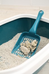 Photo of Cat litter tray with filler and scoop on floor indoors, closeup