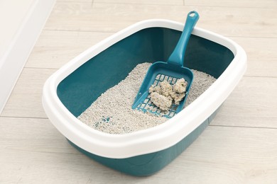 Photo of Cat litter tray with filler and scoop on floor indoors