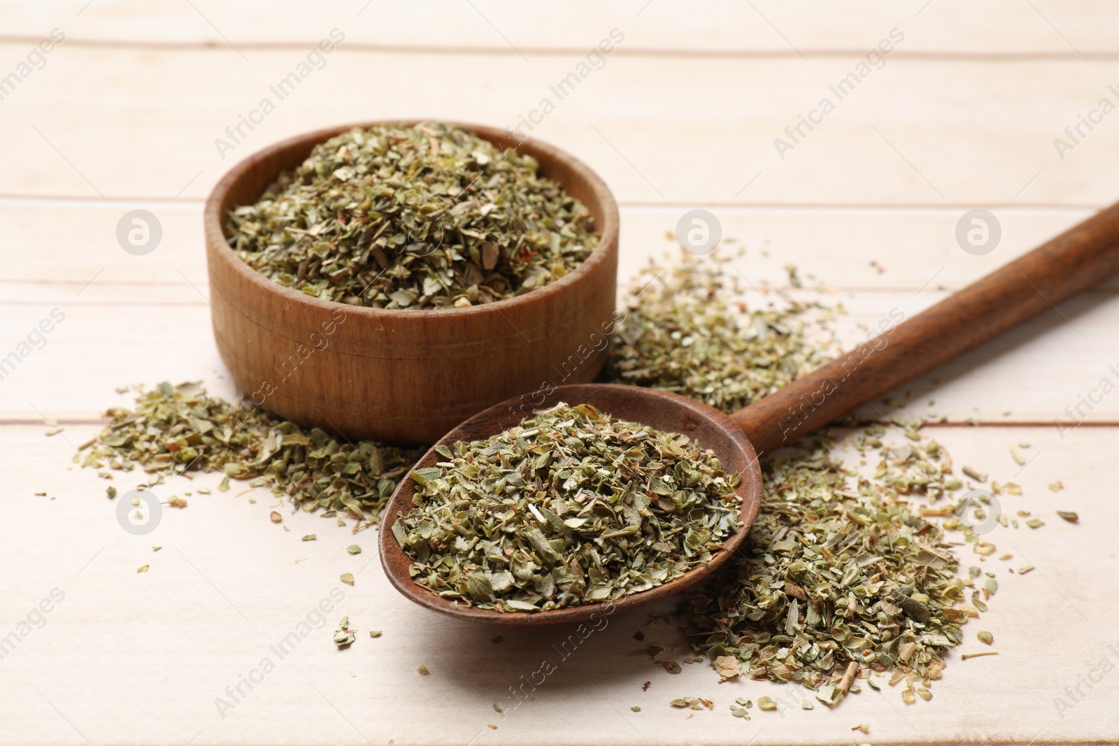 Photo of Dried oregano in spoon and bowl on wooden table, closeup