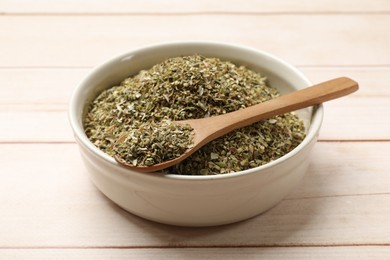 Photo of Dried oregano in bowl and spoon on wooden table, closeup