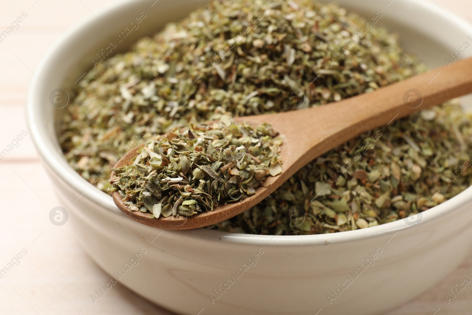 Photo of Dried oregano in bowl and spoon on table, closeup